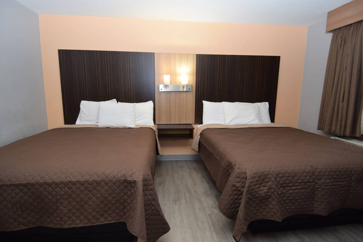 Habitación de hotel con dos camas, cabecera de madera, luz empotrada en la pared y ventana con cortinas.