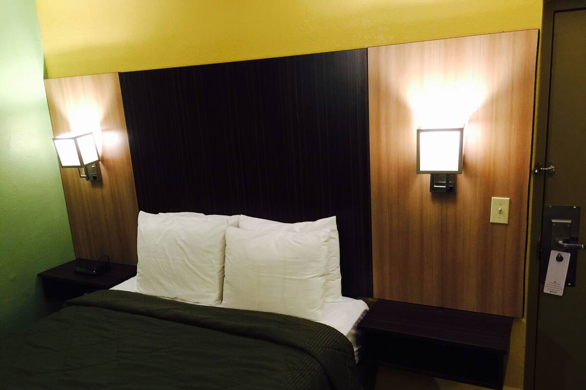 Habitación de hotel con cama, dos mesitas de noche y dos luces fijadas a la pared.