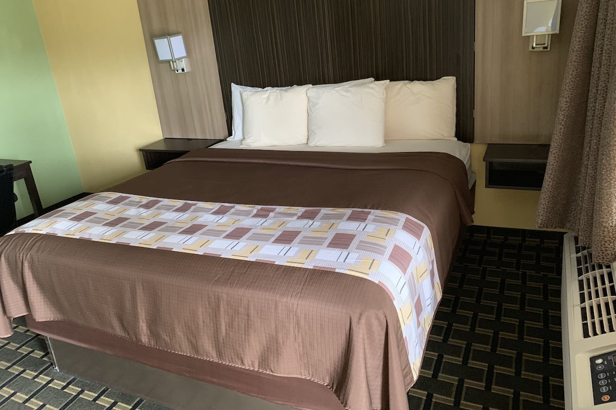 Habitación de hotel con una cama grande, cabecera, dos mesitas de noche, una lámpara de pared y una colcha estampada.