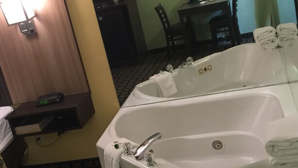A bathroom with a large bathtub, a small table with a chair, and a clock on a shelf. - University Manor Inn (Buffalo)