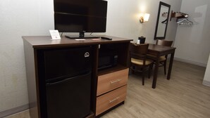 A compact hotel room with a kitchenette, a flat-screen TV, a microwave, and a small dining table with chairs. - University Manor Inn (Buffalo)