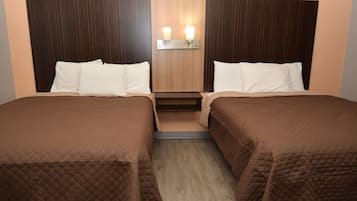 A hotel room with two beds, each with a brown quilted bedspread and white pillows. There is a wooden headboard with a light fixture above the beds.