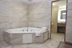 Une salle de bain moderne dotée d’une grande baignoire, de murs en marbre et d’un espace douche bien délimité.