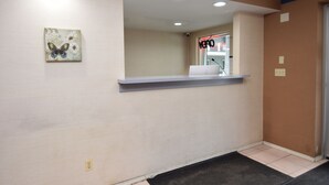 A reception area with a light-colored wall, a butterfly artwork, a reception desk, and a door with a sign. - University Manor Inn (Buffalo)