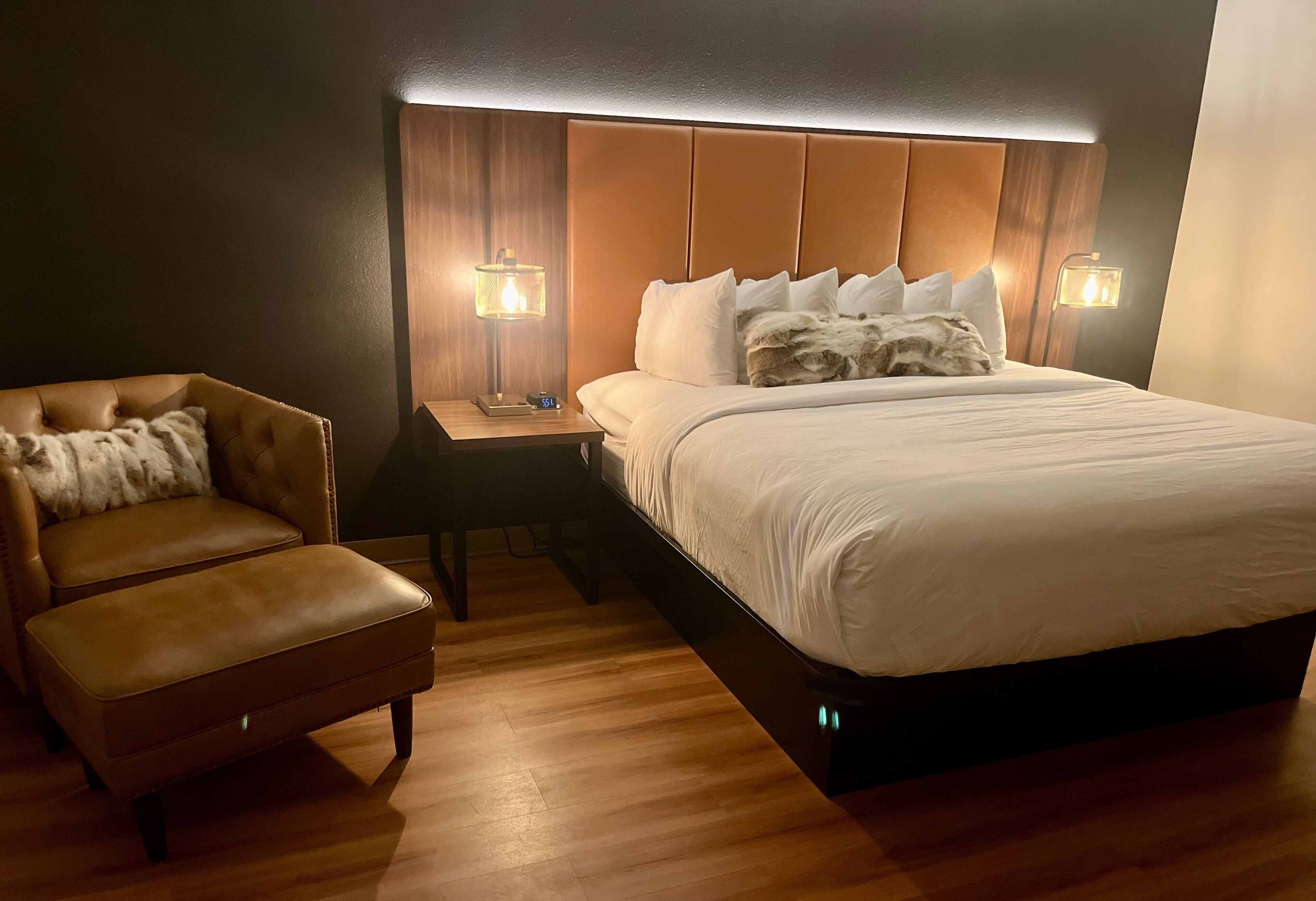 Une chambre d’hôtel avec un grand lit, un fauteuil en cuir et deux lampes de chevet.