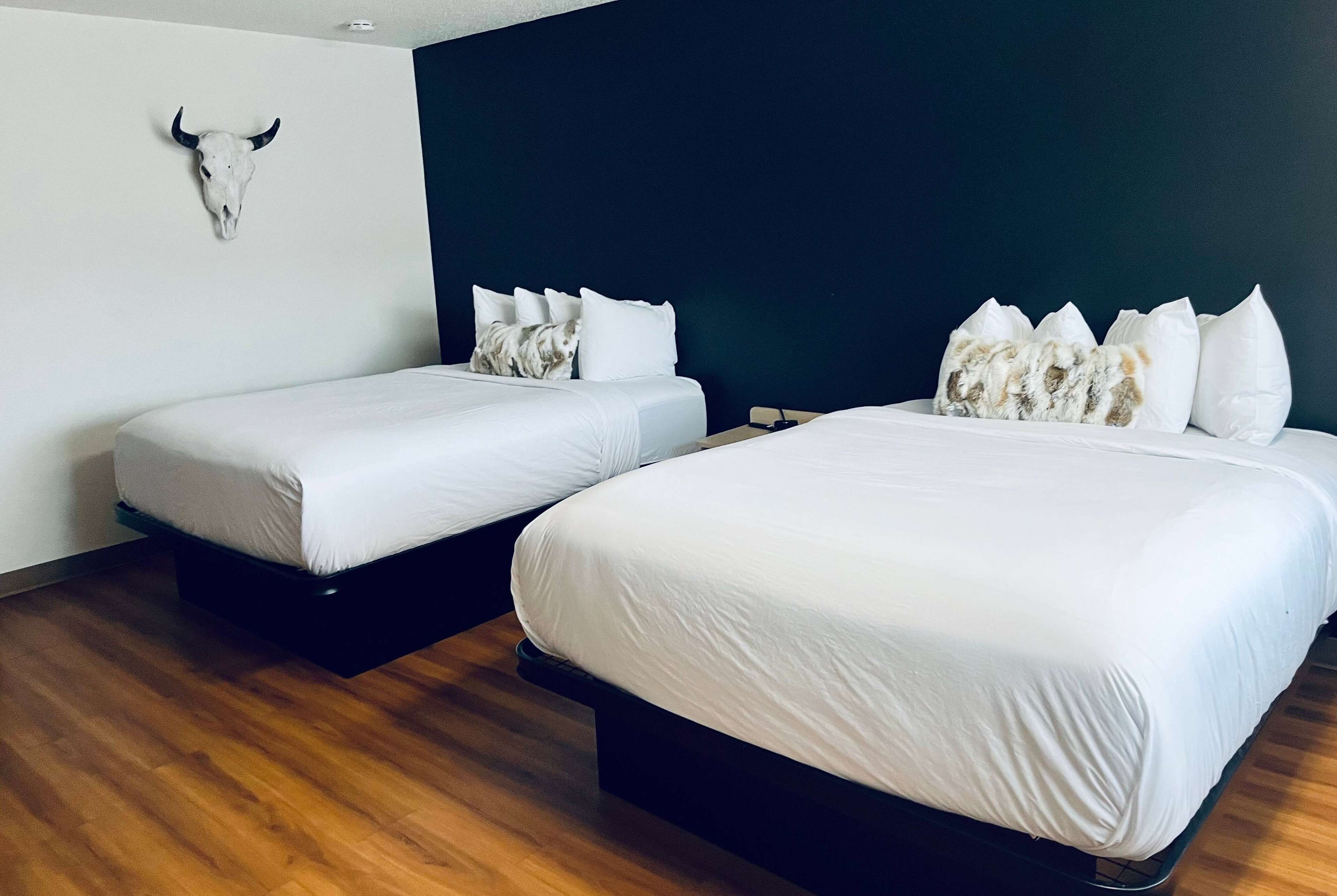 Two single beds with white bedding, a dark wall, and a wooden floor.