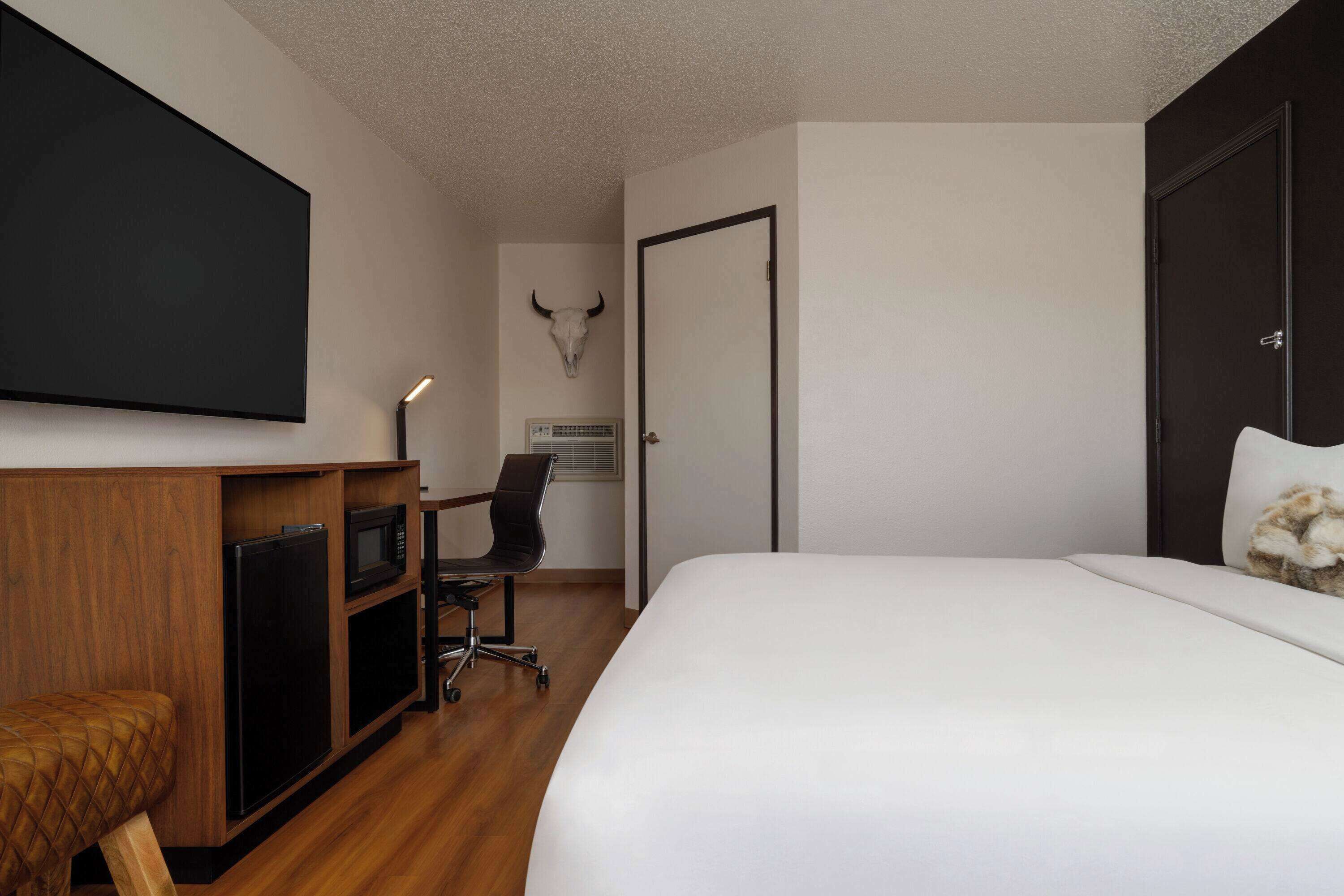 A hotel room with a bed, a desk with a chair, a television, a microwave, and a refrigerator.
