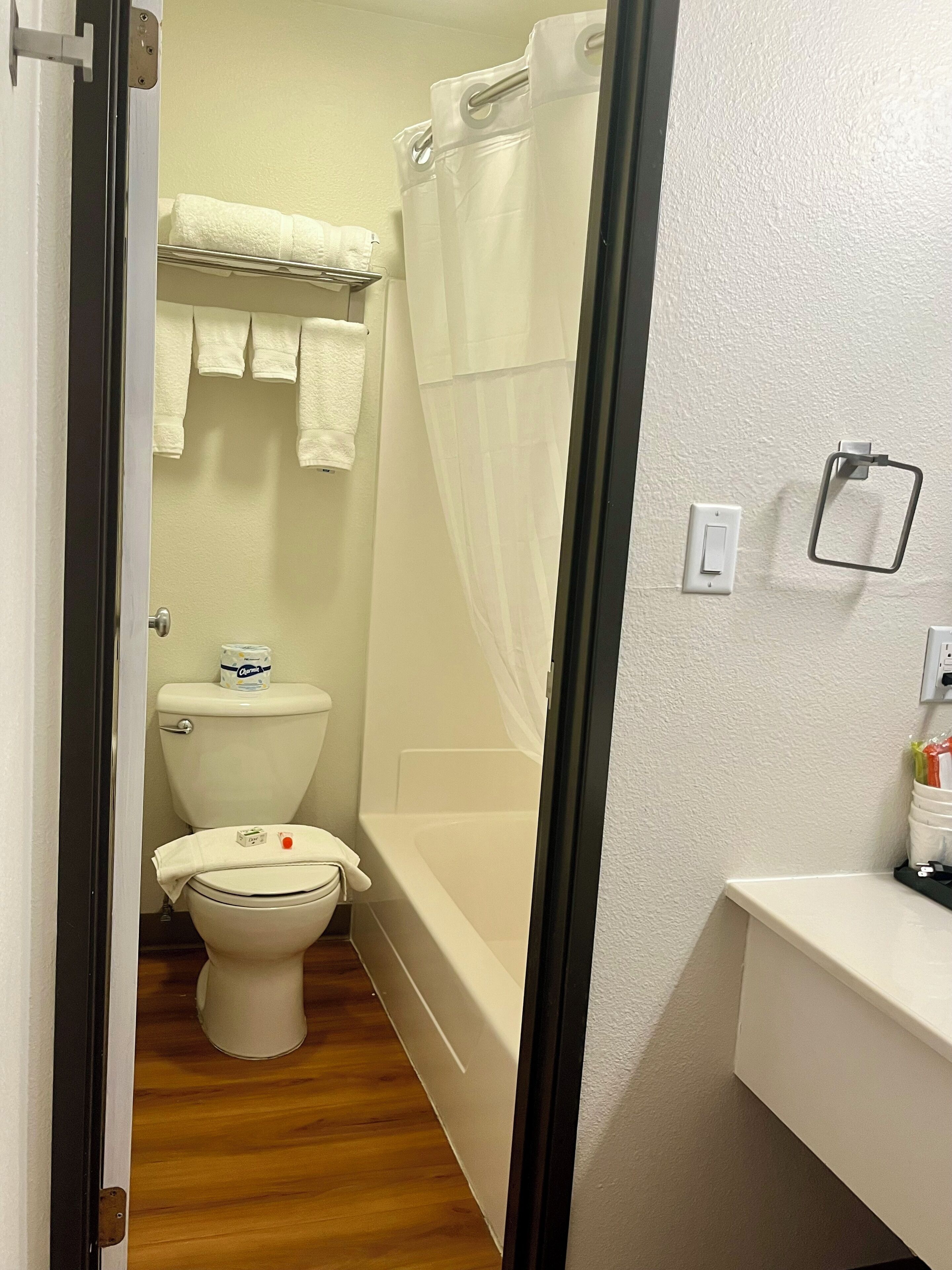 A bathroom with a toilet, a bathtub, and a shower curtain. There are towels hanging on a rack and a soap dispenser on the wall.