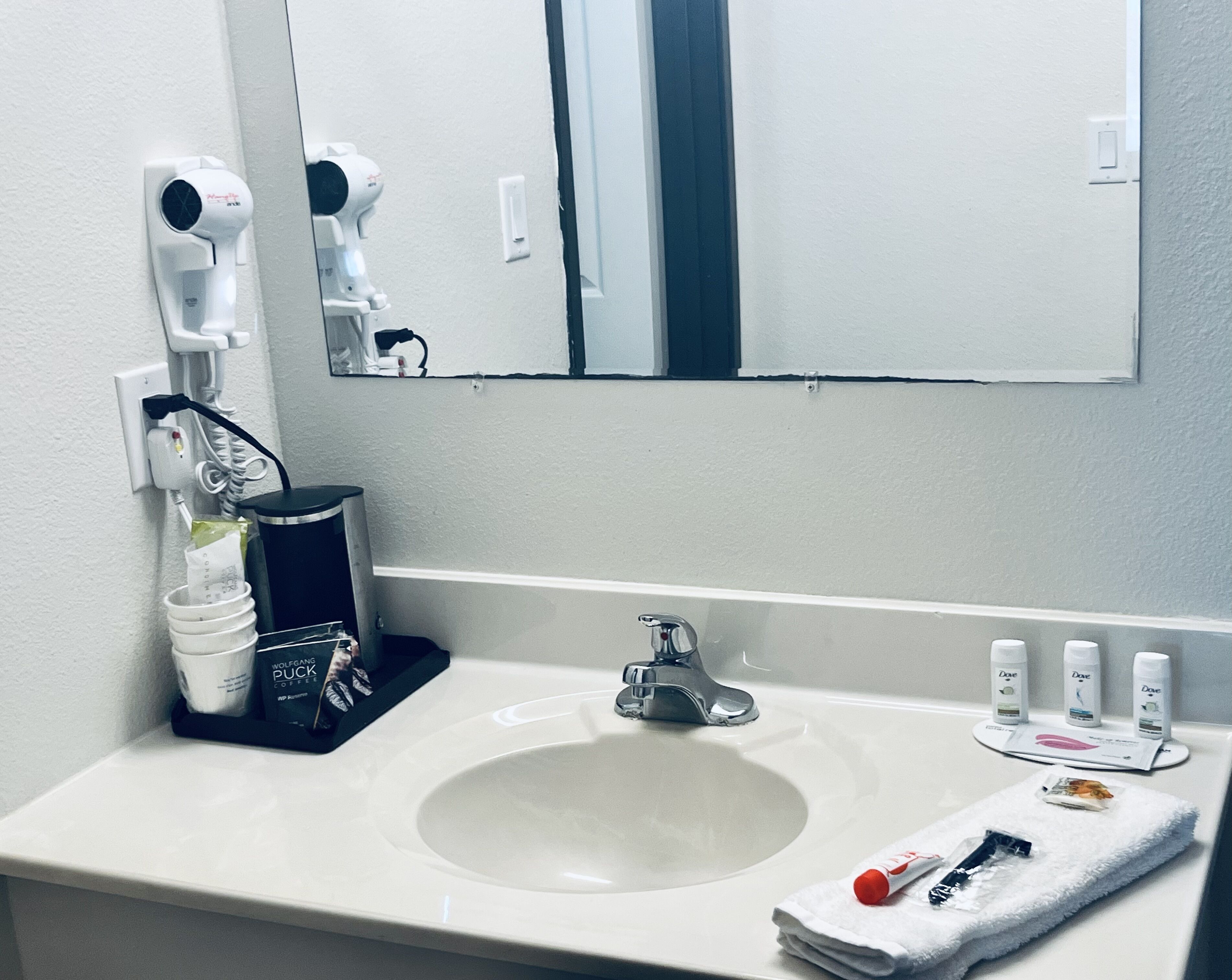 Un baño de hotel con lavamanos, espejo, secador de pelo y artículos de aseo.