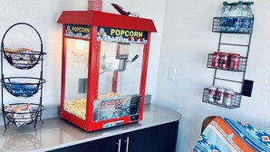 Huone, jossa on popcorn-kone, naposteltavien tuotteiden esillepano ja juomien hylly.