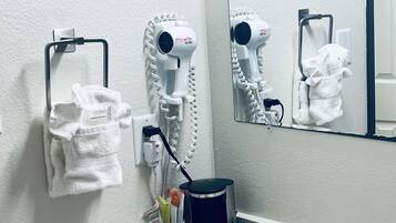 A bathroom with a towel rack, two hair dryers, a trash bin, and a coffee machine.