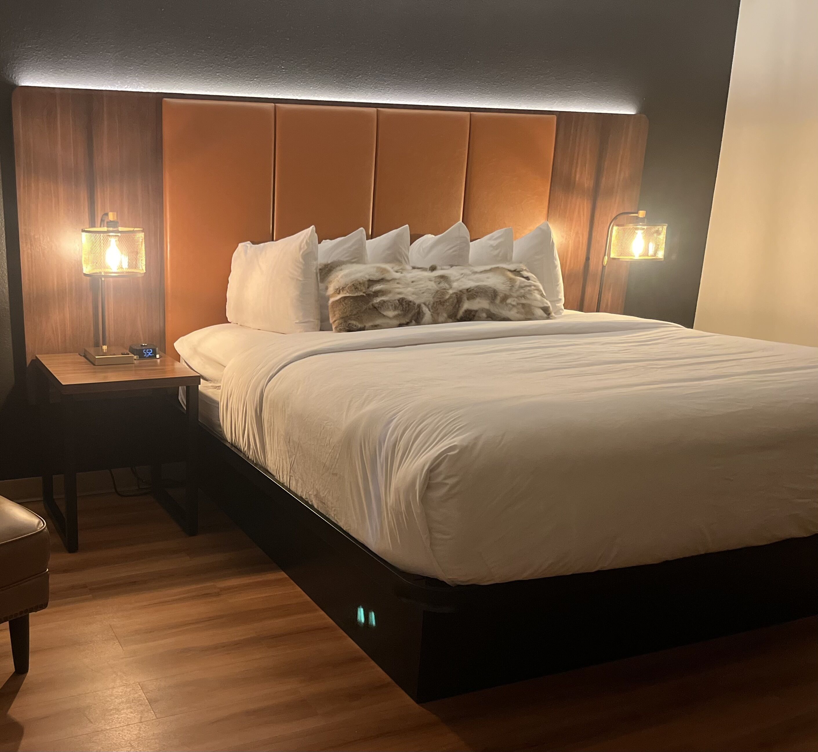 A neatly made bed with white linens, a wooden headboard, and two bedside lamps.