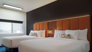 Hotellihuone, jossa on kaksi sänkyä, suuri ikkuna ja seinään kiinnitetty valaisin.