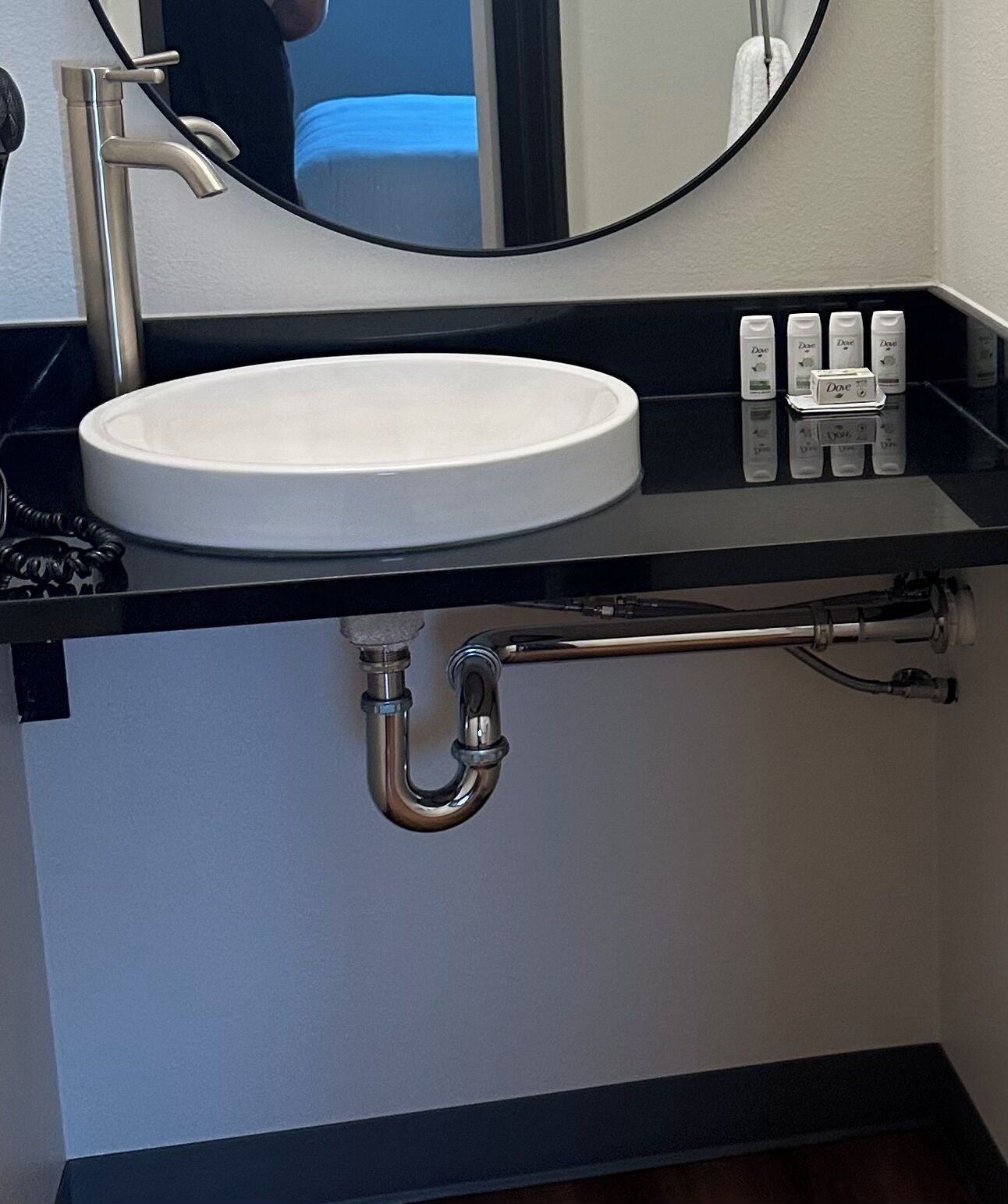 A bathroom with a white sink, black countertop, and a mirror above it.