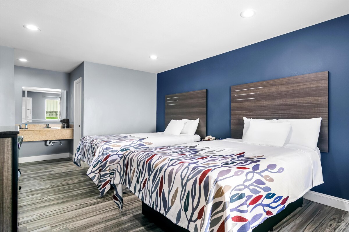 Habitación de hotel con dos camas, cabecero de madera, un espejo grande y suelo de madera.