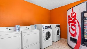 A laundry area with multiple washing machines, a Coca-Cola vending machine, and a tiled floor. - Americas Best Value Inn & Suites Siloam Springs (Siloam Springs)