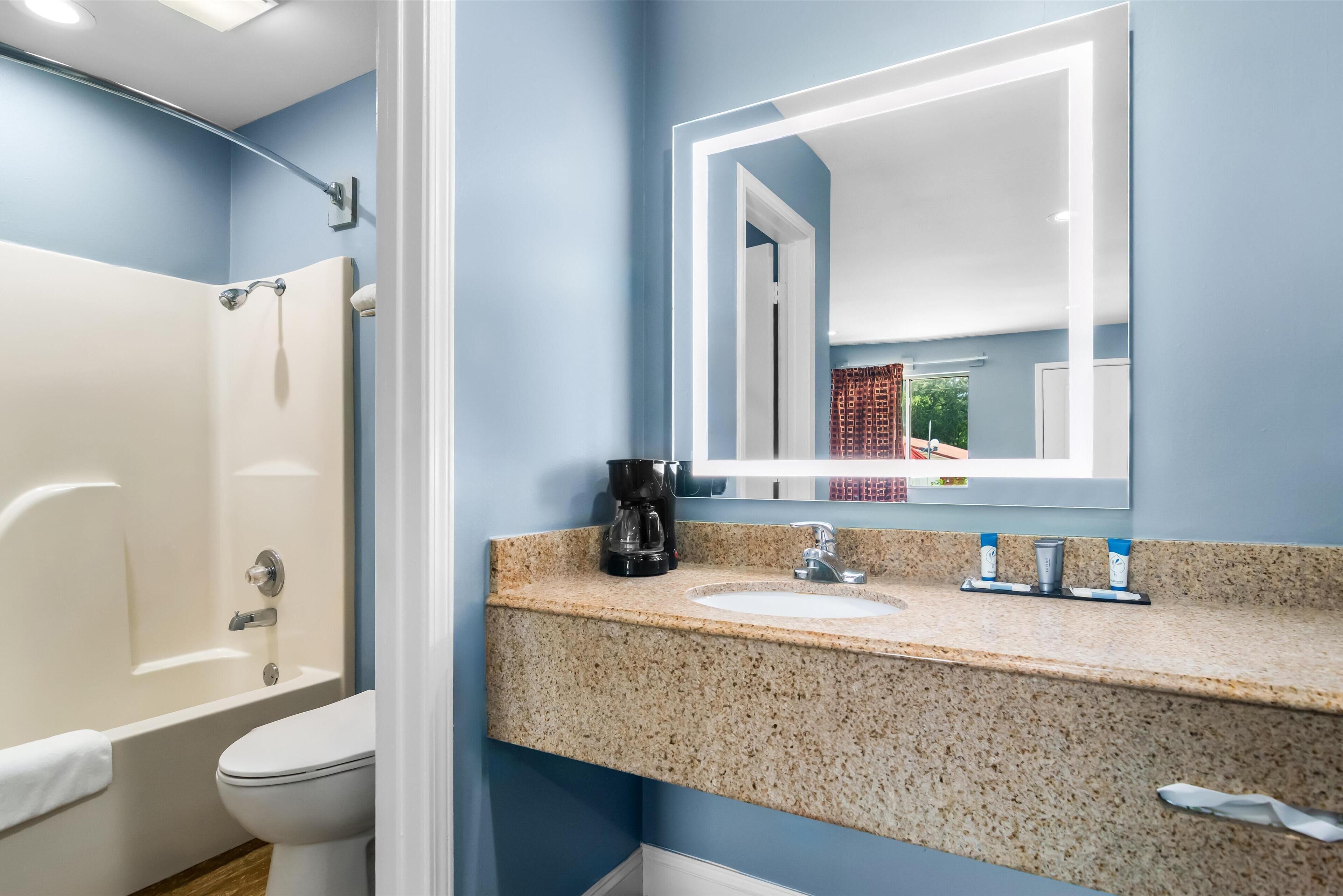 A bathroom with a white bathtub, a sink with a granite countertop, and a mirror above the sink.