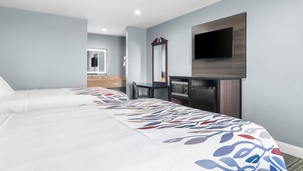 A hotel room with a bed, a desk, a mirror, and a TV mounted on the wall. - Americas Best Value Inn & Suites Siloam Springs (Siloam Springs)