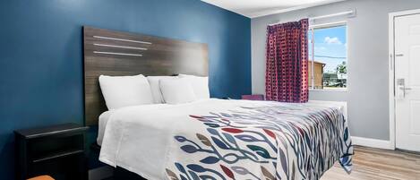 A modern bedroom with a large bed, a nightstand, a bench, and a window with curtains.