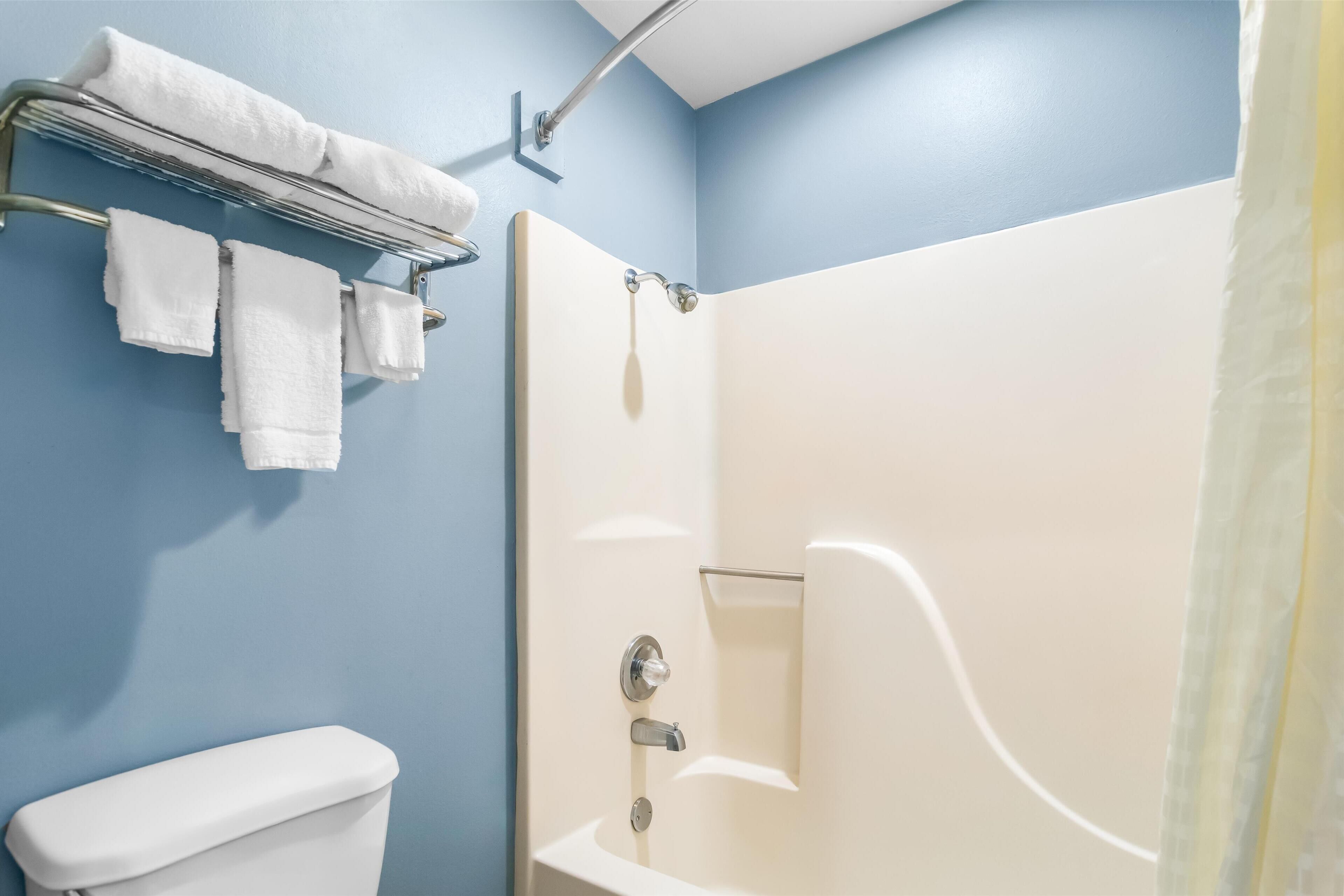 A bathroom with a white toilet, a shower with a glass door, and a towel rack with several white towels.