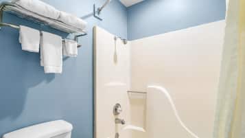 A bathroom with a white toilet, a shower with a glass door, and a towel rack with several white towels.