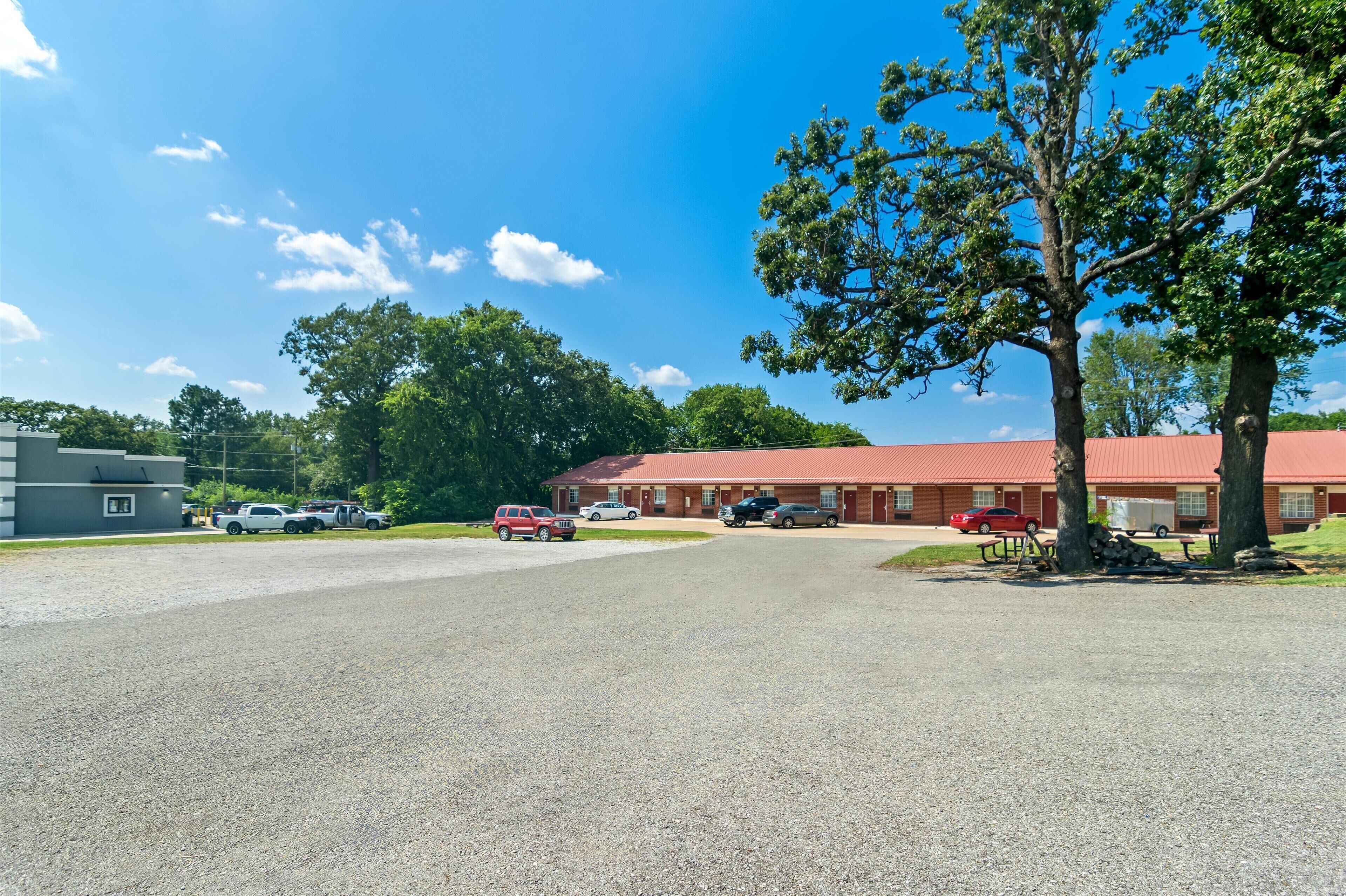 A building with a red roof, a gravel parking area, and a tree in the foreground.