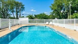 A rectangular swimming pool with a white fence, surrounded by trees and a clear sky. - Americas Best Value Inn & Suites Siloam Springs (Siloam Springs)