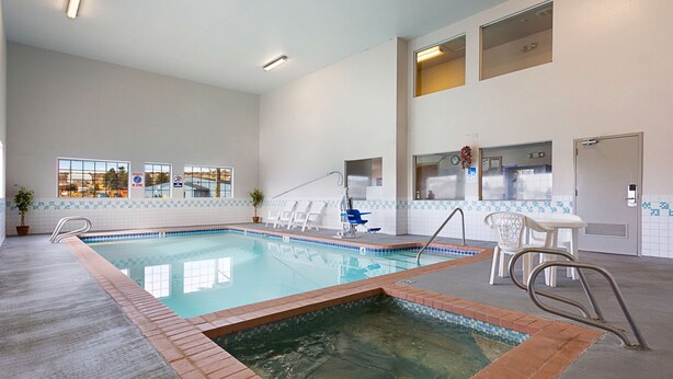 An indoor swimming pool with a tiled edge, a diving board, and a lifeguard stand. - Americas Best Value Inn Burns (Burns)