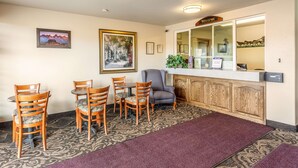 A reception area with a reception desk, a 'Welcome' sign, framed artwork, and a seating area with wooden chairs and a table. - Americas Best Value Inn Burns (Burns)
