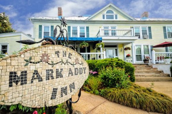Un letrero de mosaico con la leyenda "The Mark Addy Inn" frente a una casa de dos pisos con un porche y escalones que conducen a la entrada.