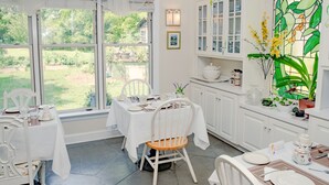 Una cocina luminosa con muebles blancos, una mesa de comedor para dos personas y vistas al jardín a través de grandes ventanales.