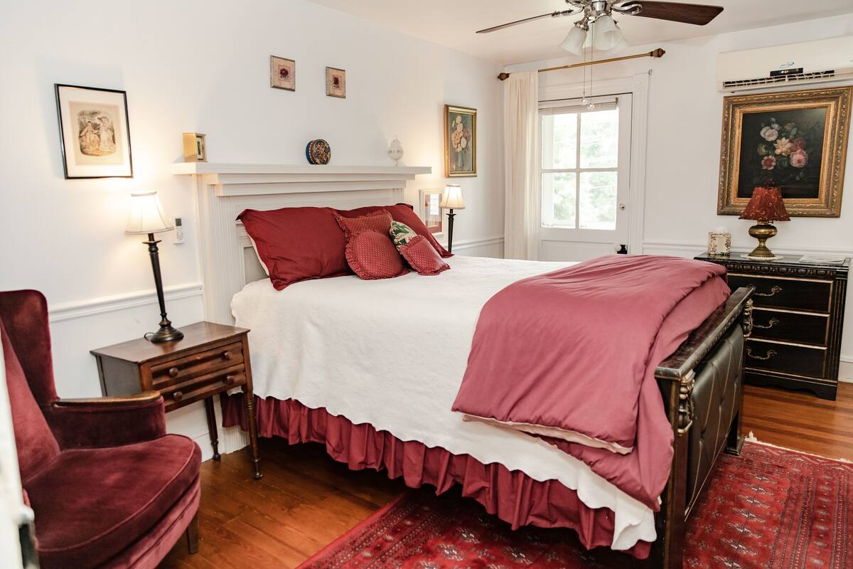 Une chambre à coucher avec un grand lit, une commode en bois, une chaise, une table de chevet et un ventilateur de plafond.