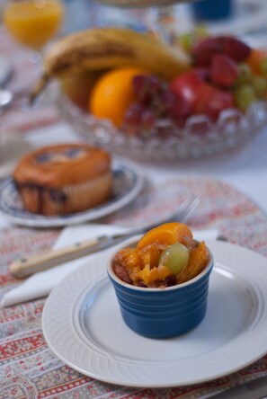 Un desayuno con un tazón de ensalada de frutas, un muffin y un vaso de jugo de naranja sobre una mesa con mantel estampado.
