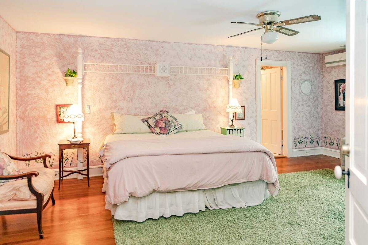 Une chambre à coucher avec un lit, des tables de chevet, une chaise, un ventilateur de plafond et une moquette verte.