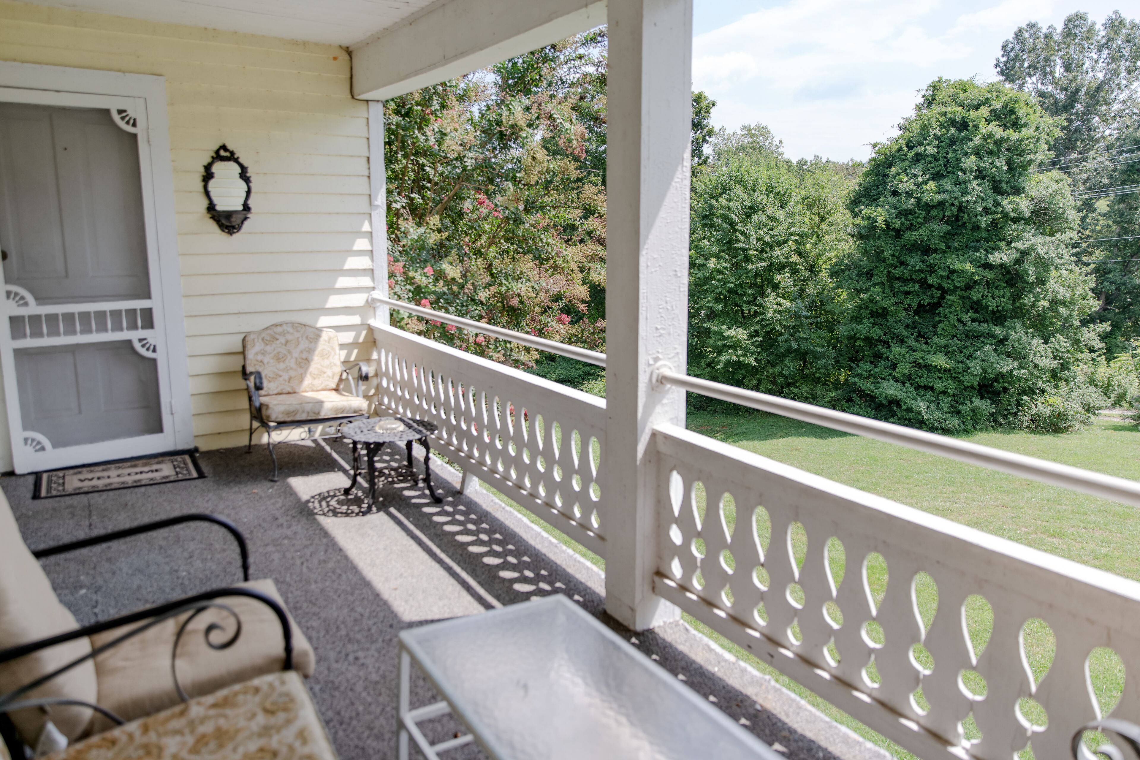 A covered porch with a white railing, a bench, and a chair.