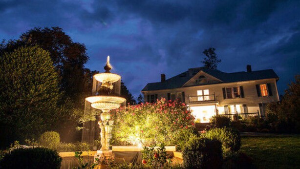 Una casa grande con un jardín iluminado y una fuente.