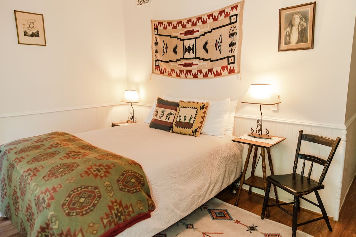 Une chambre à coucher bien rangée, avec un lit, deux tables de chevet dotées de lampes, une chaise et un tapis à motifs.