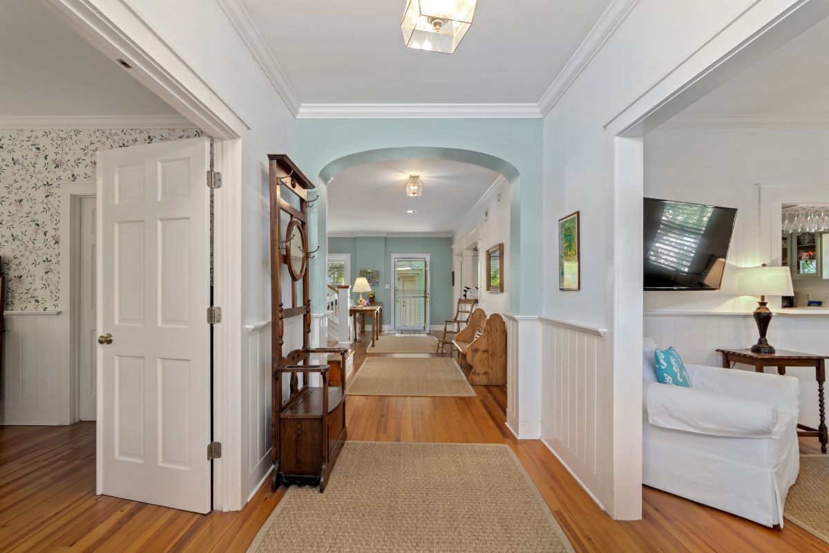 A hallway with wooden flooring, a white door, a wooden bench, a white couch, and a television on the right.