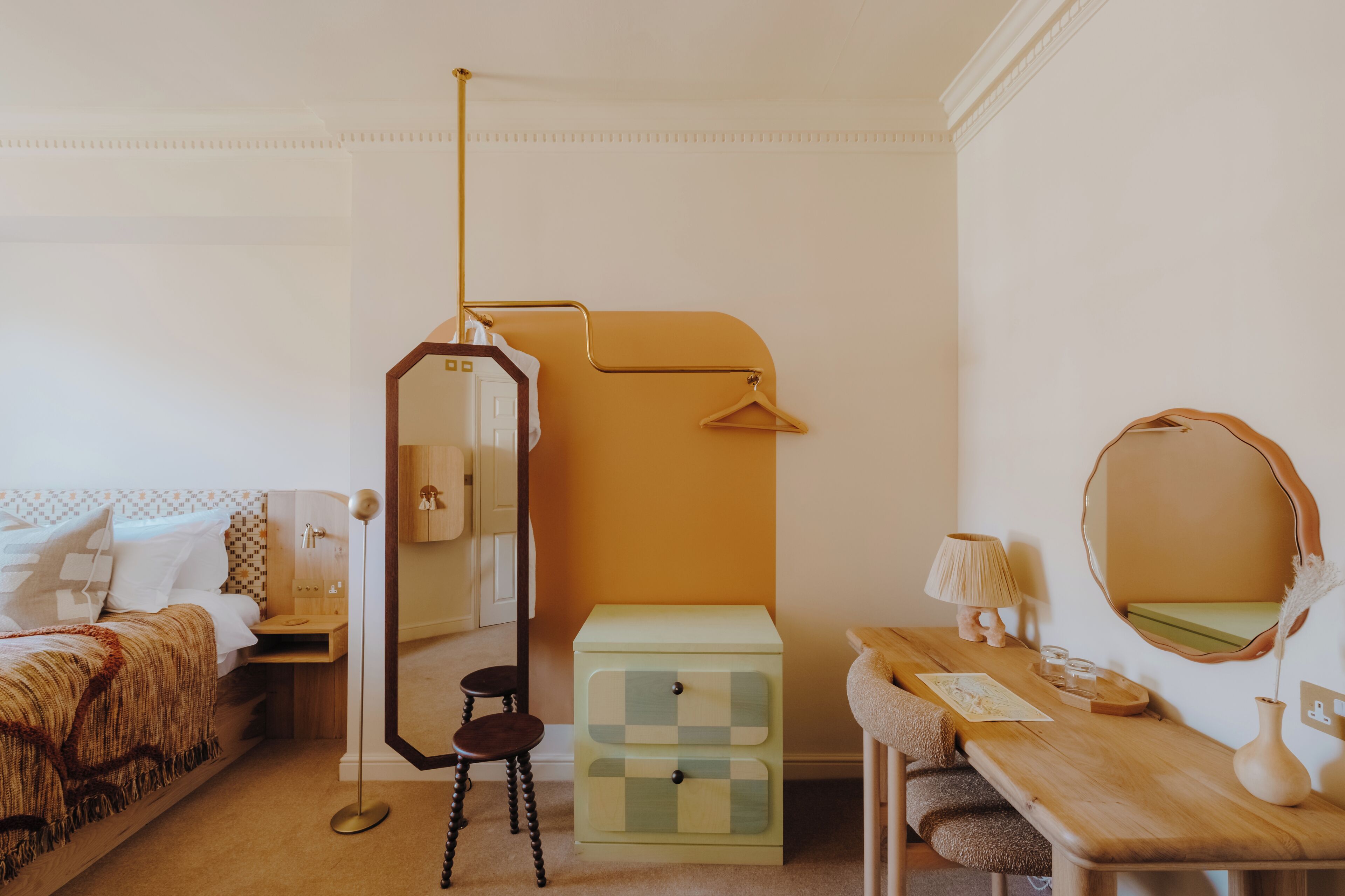 A room with a bed, a dresser, a mirror, a table with a lamp, and a hanging light fixture.