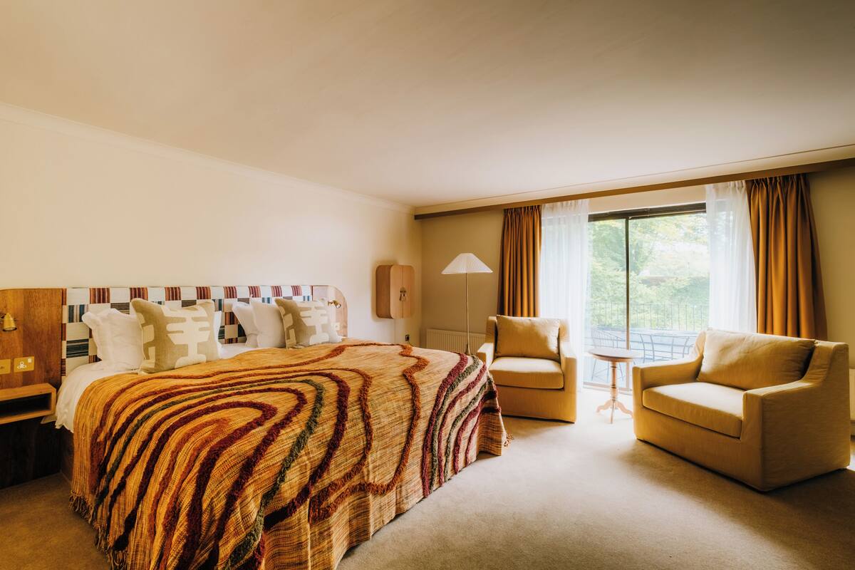 Ein Hotelzimmer mit einem Bett, zwei Sesseln, einem kleinen Tisch und einem Fenster mit Vorhängen.