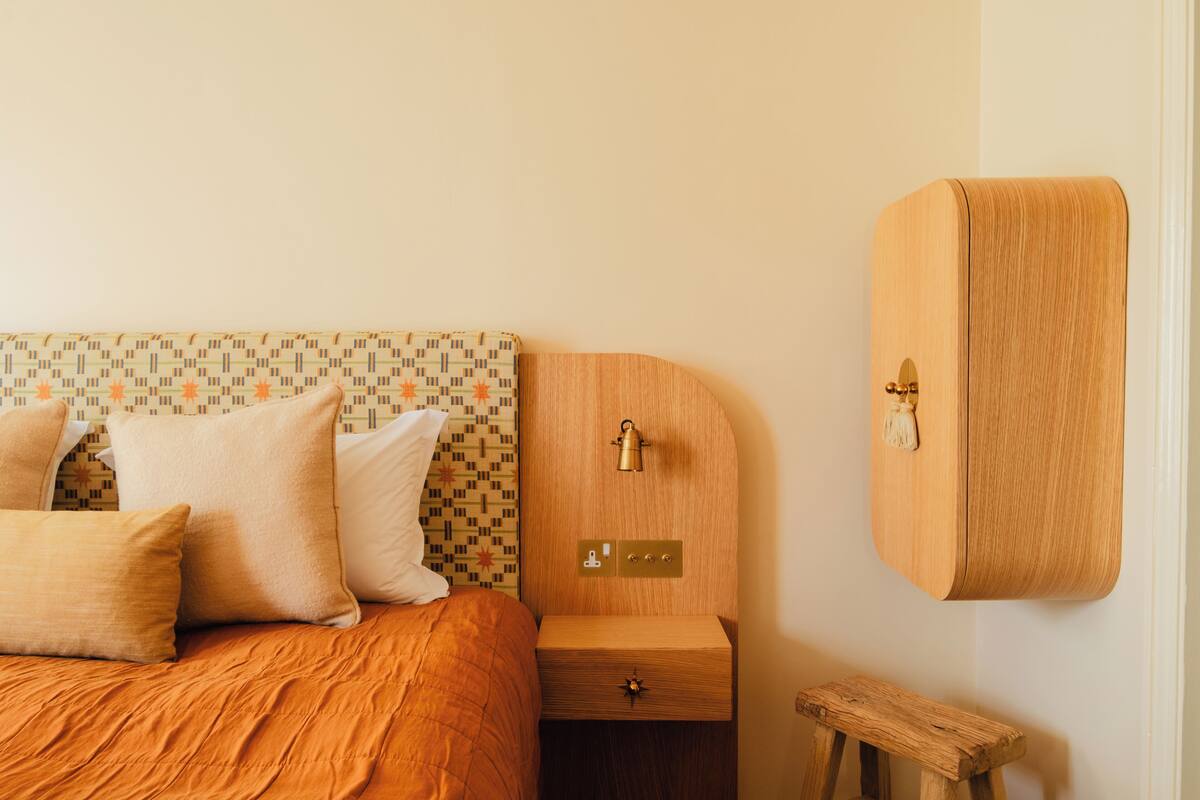 Ein Bett mit gemustertem Kopfteil, ein Nachttisch aus Holz mit Schublade und eine Holzbank.