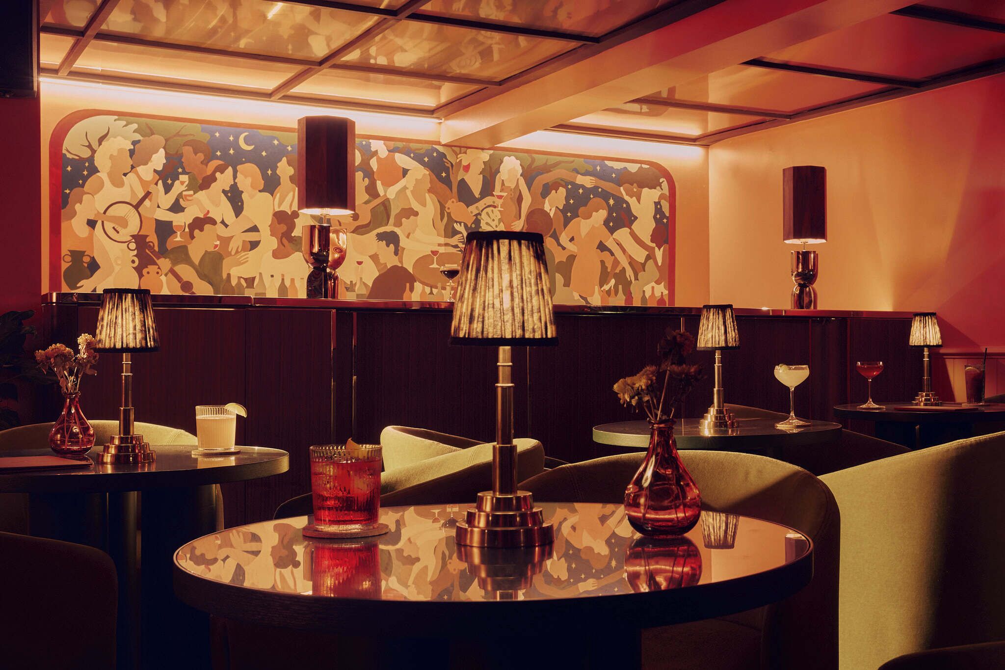 Uma área de bar com iluminação fraca, mesas redondas, banquetas de bar e luminárias decorativas.