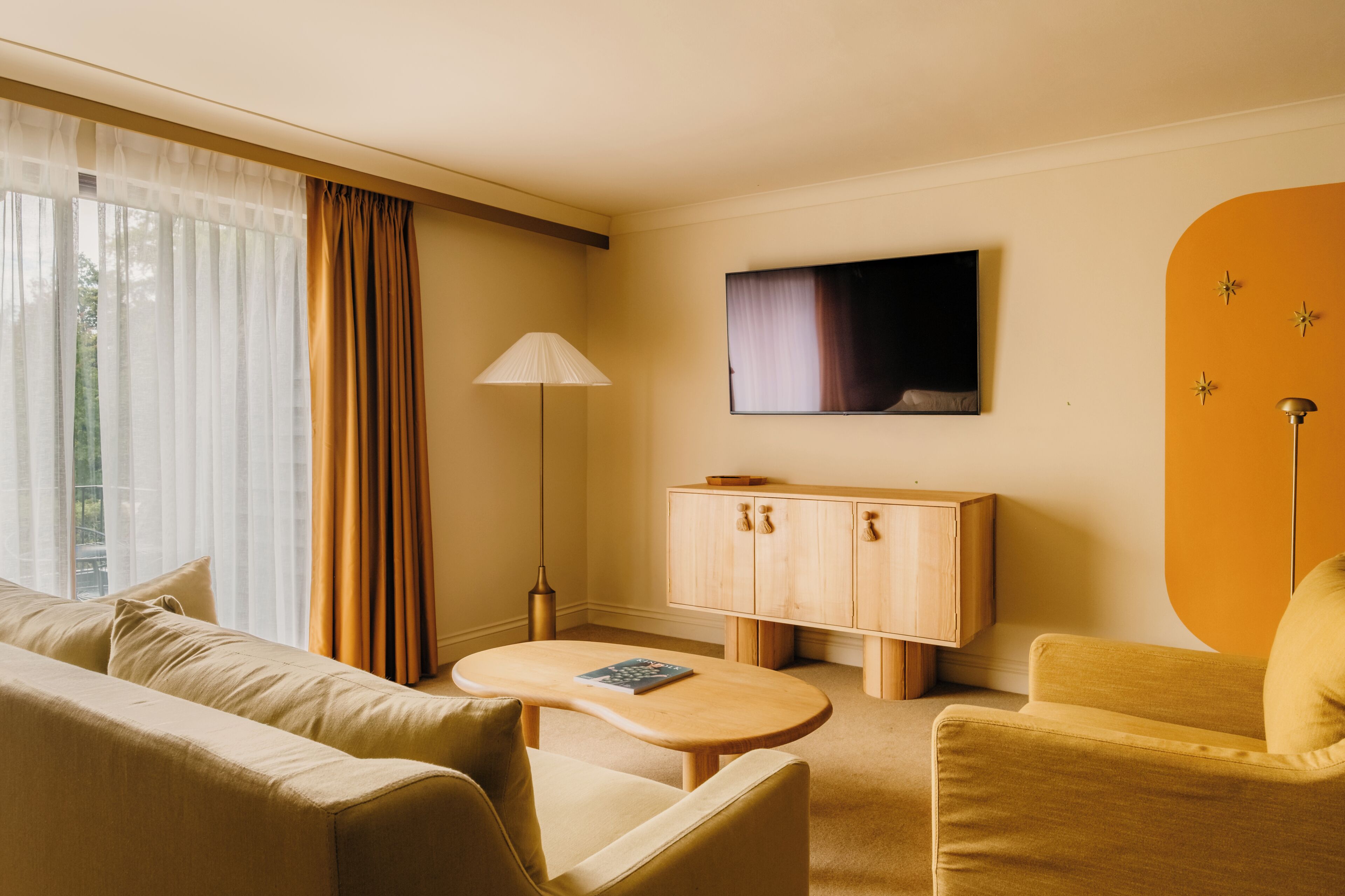 Ett hotellrum med en soffa, fåtölj, litet bord, skåp, TV och gardiner.