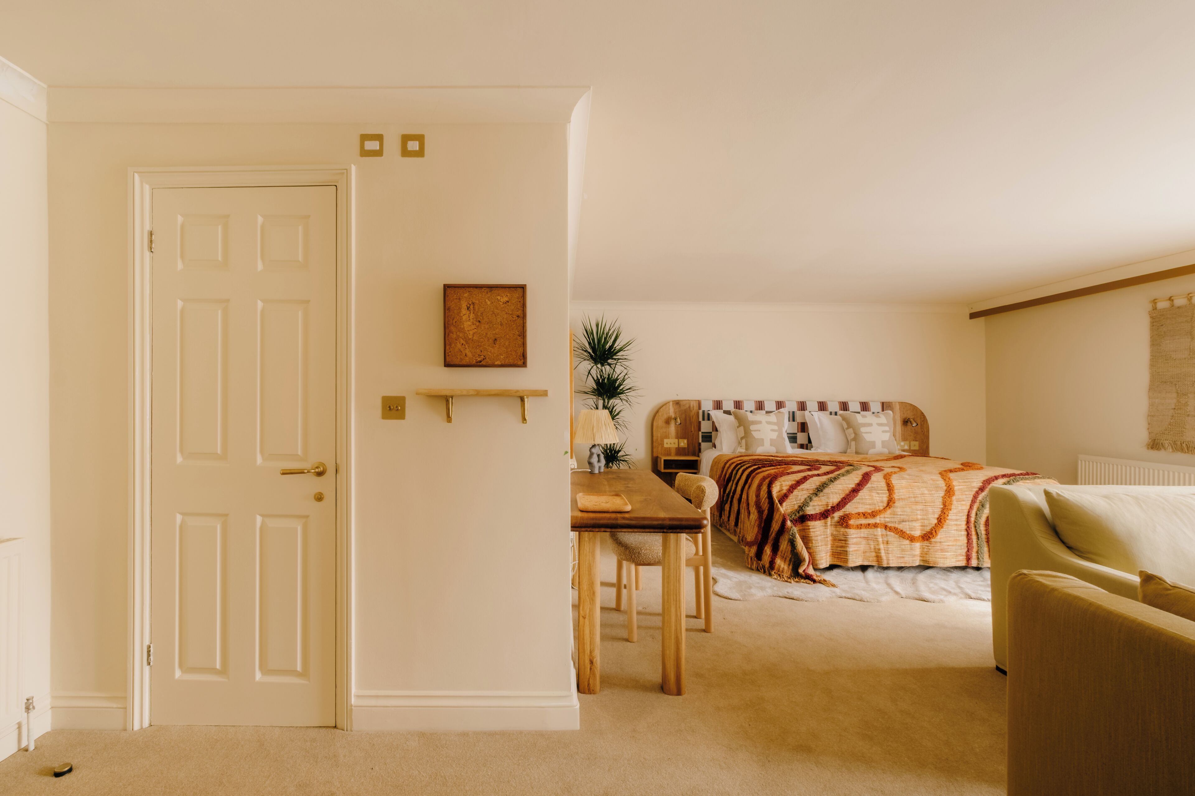A bedroom with a bed, a wooden table, a chair, and a bedside table with a lamp.