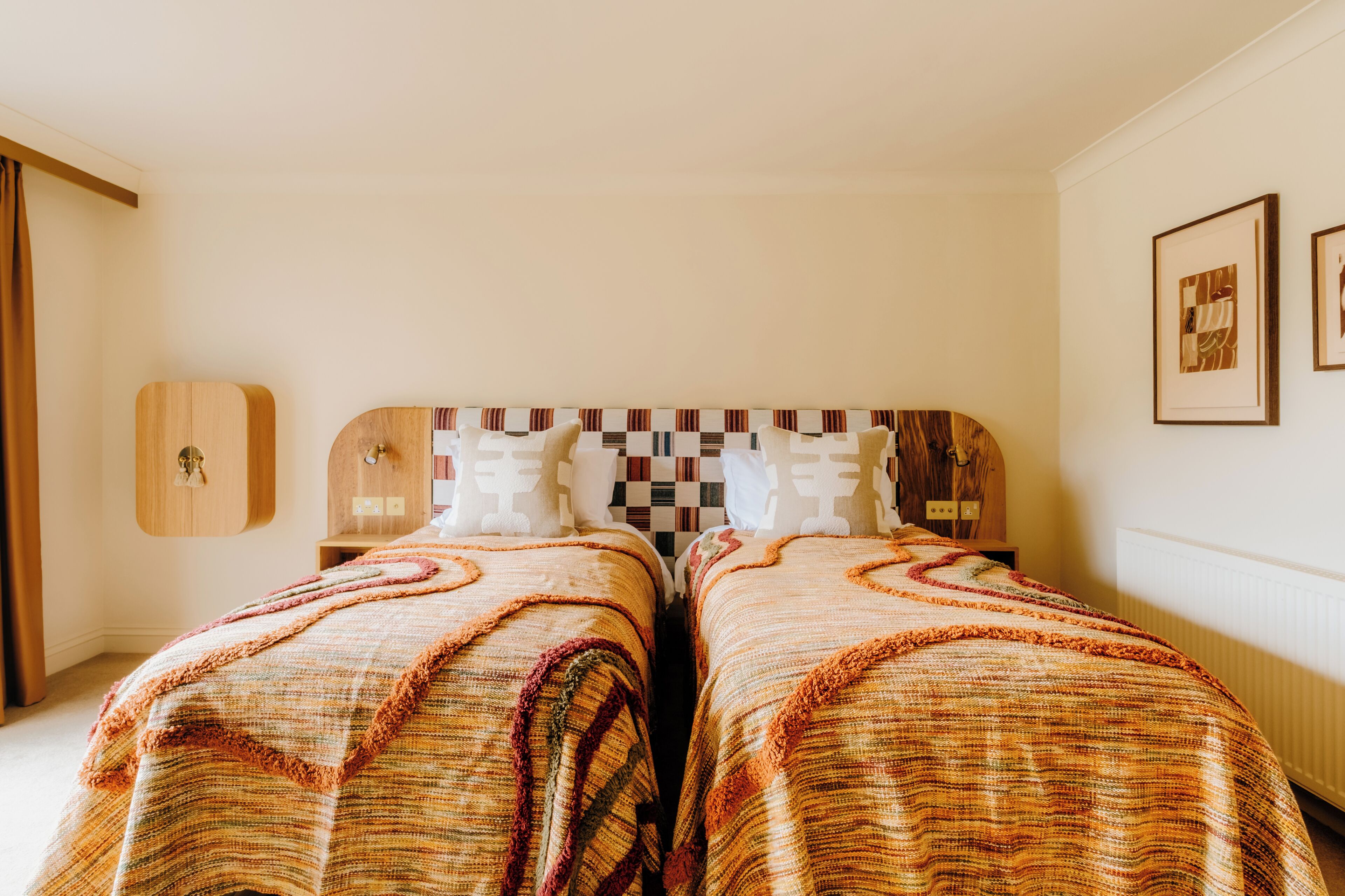 A room with two beds, a checkered headboard, and a wooden cabinet.