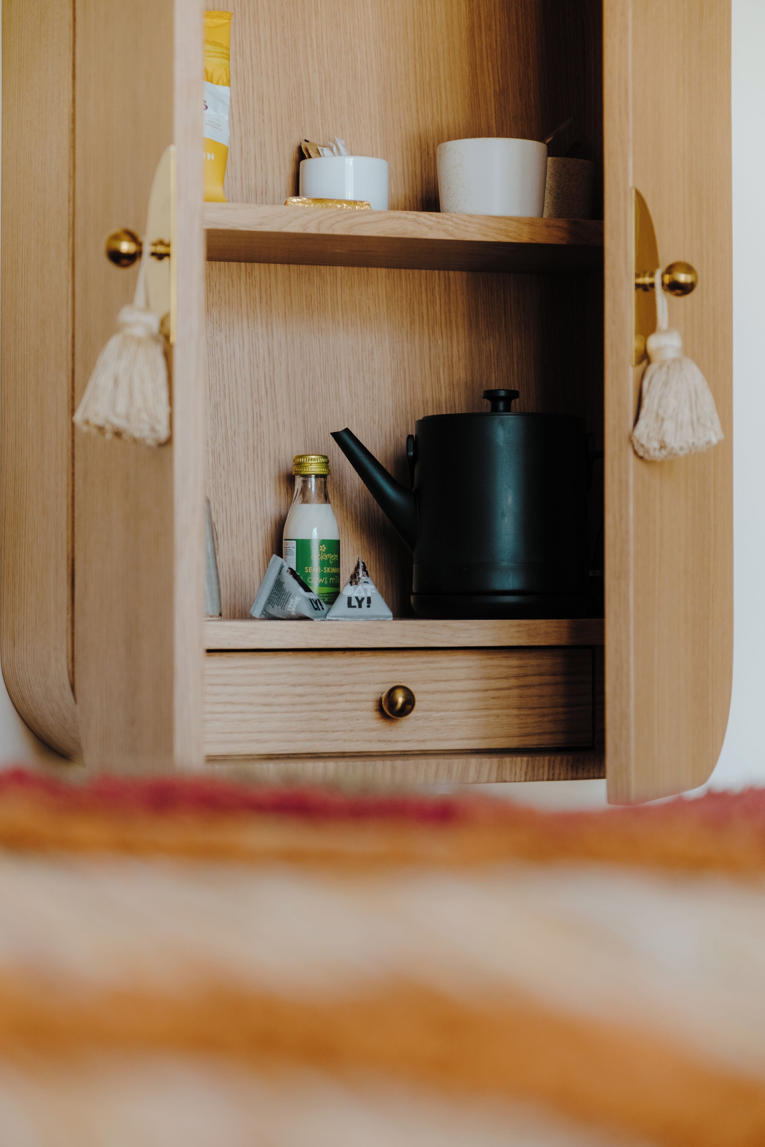 A wooden cabinet with shelves, a drawer, and a black kettle.