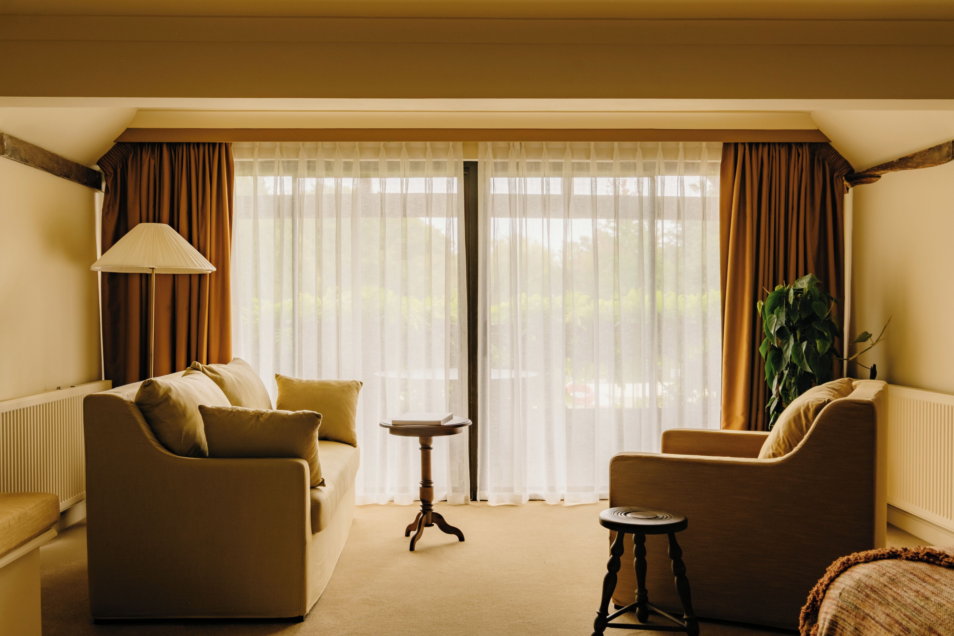 Quarto com sofá, poltrona, mesa pequena e cortinas.