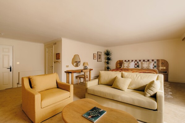 A living room with a sofa, armchair, coffee table, and a bed with a patterned headboard.