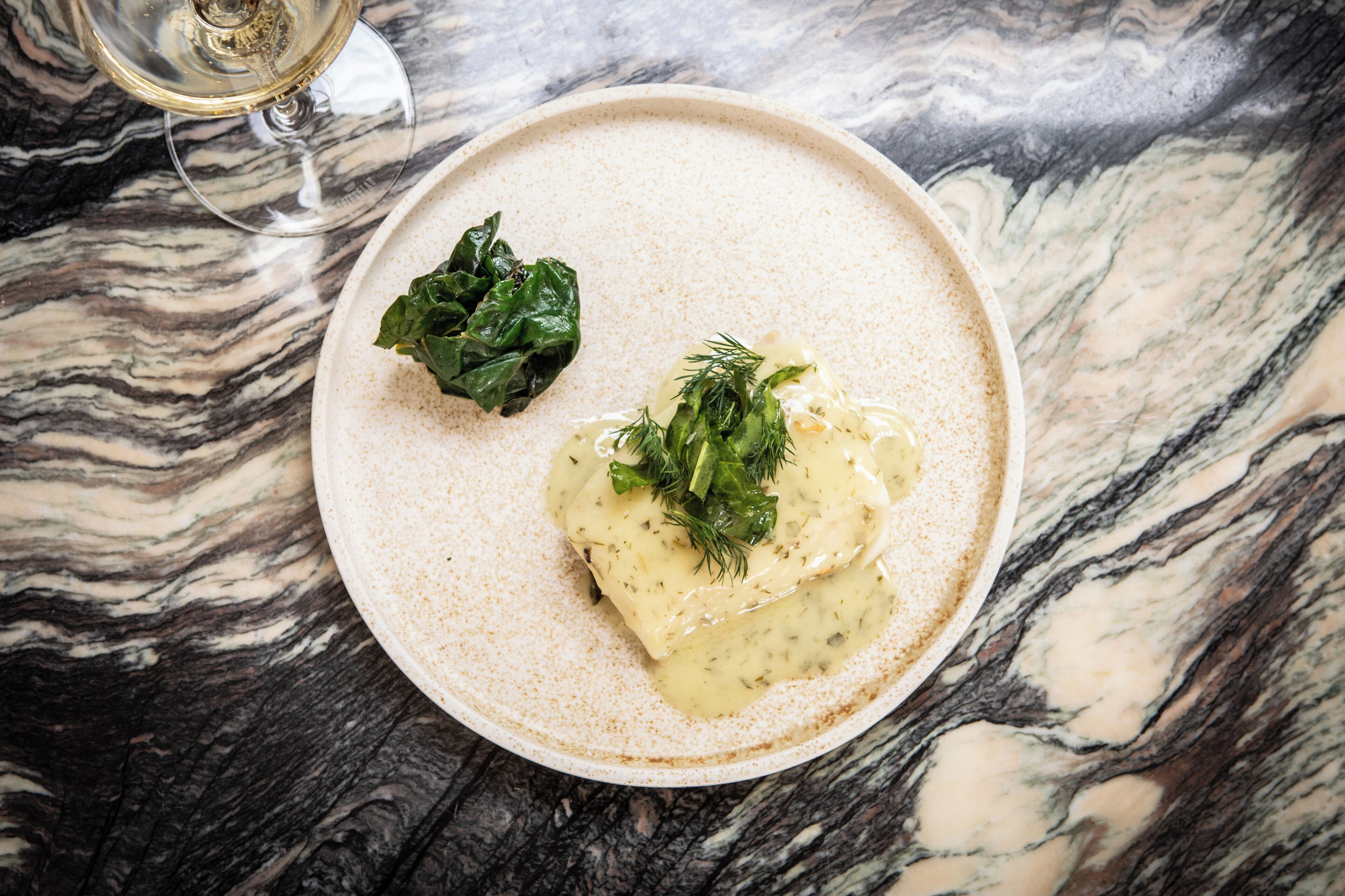 A plate of food on a marble table with a glass of white wine.