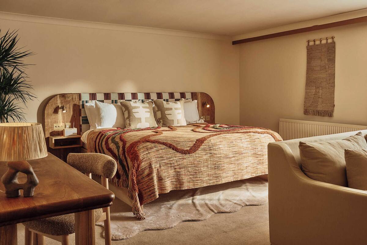 Ein Schlafzimmer mit Bett, Nachttisch, Lampe, Stuhl und einer Wandgardine.
